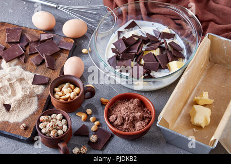 Schokolade Pound Cake aus Buchweizen Mehl, Eier, dunkle Schokolade, Nüsse, Milch und Butter. Zutaten, Schneebesen, Metall Backform auf einer konkreten Tab Stockfoto