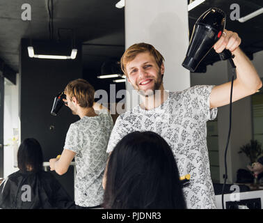 Professionelle smiling männlichen Stylist föhnen Woman's Haar mit einem Trockner im Salon Stockfoto