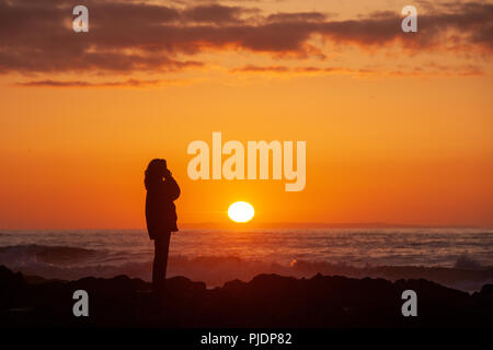Eine Frau telefoniert am Strand bei Sonnenuntergang Stockfoto