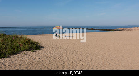 Strand am frühen Morgen mit einem gestreiften Schirm und Fischer in der Ferne auf felsigen Pause Stockfoto