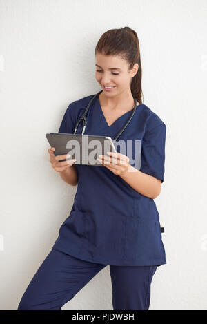 Junge Frau Arzt oder Krankenschwester in Blau scrubs Holding ein Tablet PC vor einer weißen Wand Stockfoto