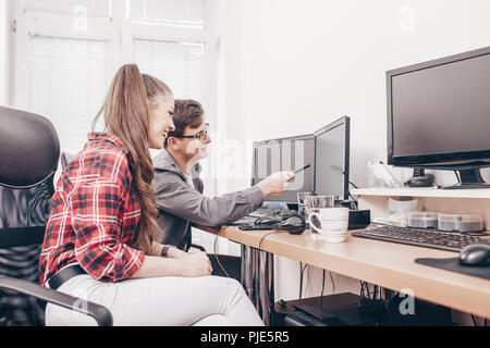 Zwei lächelnde Kollegen reden, während an einem Schreibtisch in einem Büro arbeiten online auf Desktop Computern sitzen Stockfoto