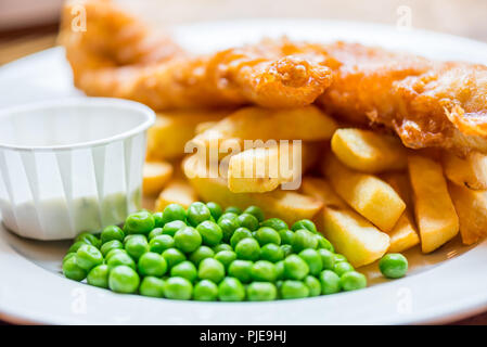 Traditionelle englische Lebensmittel wie Fisch und Chips mit grünen Erbsen in der Kneipe oder im Restaurant serviert. Stockfoto