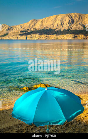 Ein einsamer Sonnenschirm am Strand bei Tagesanbruch am Wasser der Adria in Baska auf der Insel Krk in Kroatien Stockfoto