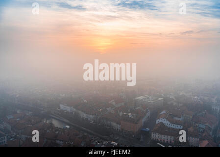 Bunte winter Sonnenuntergang durch den Nebel über der Stadt Ljubljana, Hauptstadt Sloweniens, Luftaufnahme, an einem kalten Tag im Dezember. Stockfoto