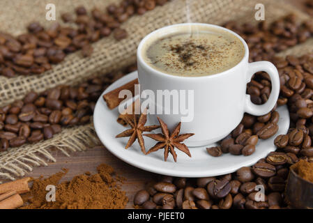 Tasse Kaffee mit Gewürzen auf dem Hintergrund der Kaffeebohnen Stockfoto