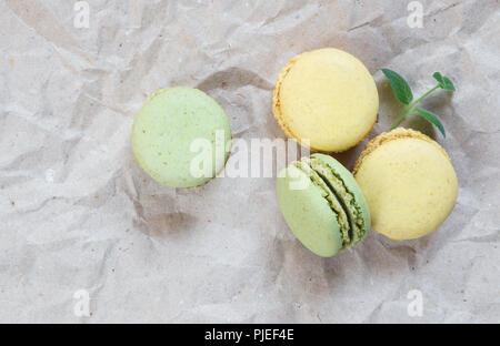 Grün und Gelb almond Cookies (makronen) und grüne Minze auf dem Hintergrund der zerknitterten Handwerk Papier; Ansicht von oben, flach Zusammensetzung Stockfoto