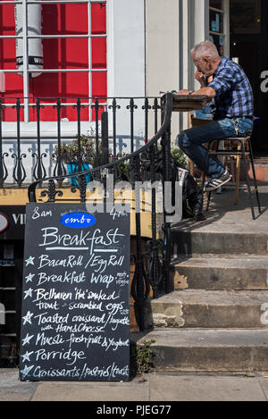 Ein reifer Mann sitzt in der Sonne draußen ein Cafe am Leith Walk zu frühstücken. Stockfoto