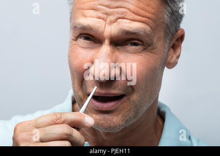 Nahaufnahme einer reifer Mann in den Schmerz Entfernen von Haaren in Nase mit einer Pinzette Stockfoto