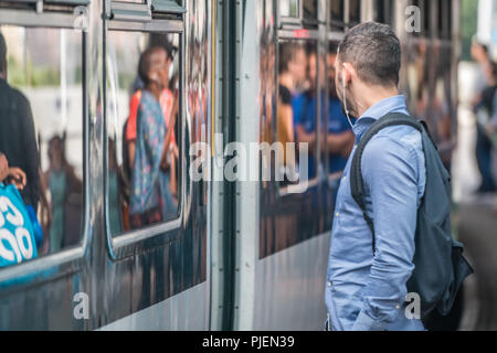 London, England - Juli 2018: der Mann, der das Hören von Musik über Kopfhörer beim Warten auf die S-Bahn anreisen, auf der Plattform, Großbritannien Stockfoto