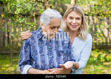 Deaktiviert alte Dame unter medizinische Pillen aus der freundliche Helfer Hand. Die Zeit im Garten Stockfoto