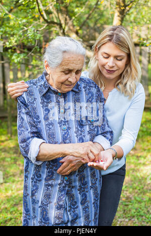 Deaktiviert alte Dame unter medizinische Pillen aus der freundliche Helfer Hand. Die Zeit im Garten Stockfoto