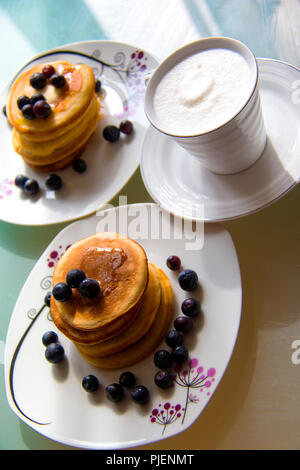 Wüste mit Kaffee, süße Pfannkuchen mit Ahornsirup und Heidelbeeren auf dem stilvollen Platten, weiße Creme Kaffee Stockfoto