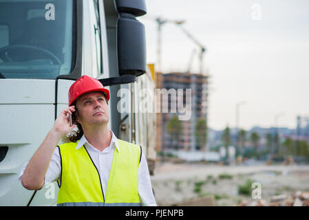 Lkw-Fahrer über sein Mobiltelefon auf einer Baustelle Stockfoto