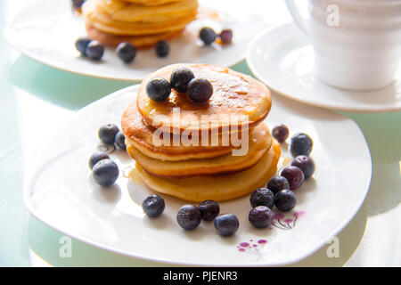 Leckere hausgemachte Pfannkuchen mit Ahornsirup und organischen Blaubeeren auf dem weißen Teller weiter die Tasse Kaffee. Süßes Frühstück Pfannkuchen Stockfoto