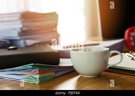 Nahaufnahme von einer Tasse Kaffee und Bürobedarf auf dem Schreibtisch im Büro am Morgen, warmen Ton Stockfoto