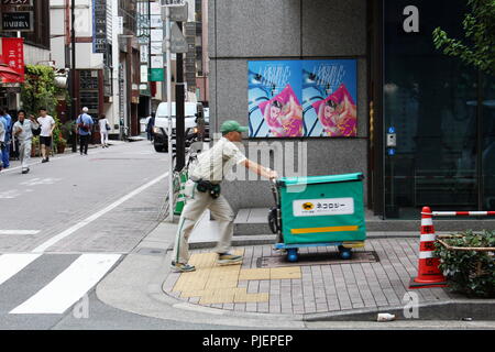 Ein Yamato Transport Company (kuroneko) zu Fuß Lieferung Arbeiter schiebt mit Karre auf einem Bürgersteig vor der Galerie GGG in Tokyos Ginza District. Stockfoto