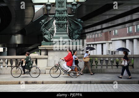 Fußgänger und Radfahrer pass Statuen von Drachen auf Nihonbashi Brücke. Die shoto Expressway ist oberhalb der Brücke. (Juni 2018) Stockfoto