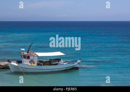 Griechenland, die charmante, kleine Insel Koufonissi. Ein traditionelles Fischerboot aus Holz, das an einem kleinen Steg auf dem kristallklaren, blauen Ägäischen Meer festgemacht ist. Stockfoto