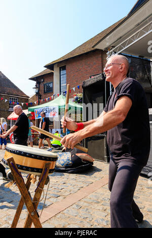 Englisch Gruppe, kaukasischen Männern Kensei Taiko, die traditionelle japanische Trommeln im Sandwich Town Square. Tagsüber, Sonnenschein. Seite Weitwinkelaufnahme. Stockfoto