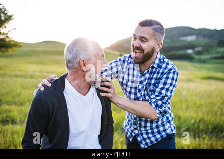 Ein erwachsener Sohn Hipster mit Senior Vater auf einem Spaziergang in der Natur bei Sonnenuntergang, Spaß zu haben. Stockfoto