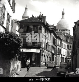 1950 s, historischen, einen Blick auf die rue Norvins, einer Straße mit Kopfsteinpflaster im Pariser Viertel Montmartre, berühmt für seine Künstler und zeigt das verfallende Gebäude der alten Pariser Café, Le Consulat und im Hintergrund, die Kuppeln der der Römisch-katholischen Kirche Sacre-Coeur. Die klassische französische Auto, der Citroen 2CV in der pciture gesehen werden kann. Stockfoto