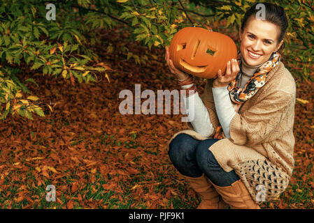 Trick oder Festlichkeit. glückliche junge Frau auf Halloween im Park mit Kürbis Jack O'Lantern Stockfoto