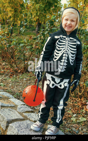 Trick oder Festlichkeit. glückliches Kind tragen Skelett Kostüm für Halloween im Freien holding Kürbis Jack O'Lantern Warenkorb Stockfoto