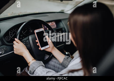 Business Frau im Auto sitzen und über Ihr Smartphone. Mockup Bild mit weiblichen Fahrer- und Verbindungsmenü Stockfoto