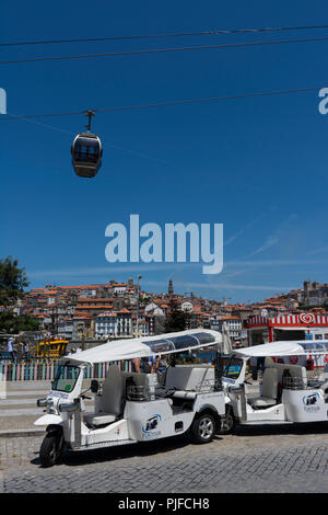 VILA NOVA DE GAIA, PORTUGAL - 21. JULI 2017: Geparktes touristisches Tuk-Tuk in Gaia, am Ufer des Douro, unter der Seilbahn. Porto im Hintergrund Stockfoto