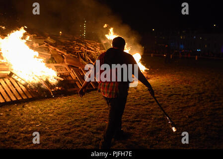 Ein Mann hält eine Fackel Spaziergänge vor einem brennenden Feuer während der Nacht am Lagerfeuer feiern am 5. November in Petworth, West Sussex. Stockfoto
