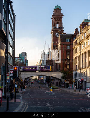 Manchester, England, UK - 30. Juni 2018: Eine nördliche Bahn Klasse 323 elektrische S-Bahn überquert von Manchester Oxford Road, mit dem Glockenturm von t Stockfoto