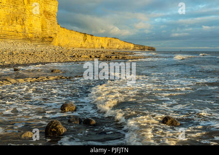 Der Glamorgan Heritage Coast in Llantwit Major Beach, South Wales am Abend mit der Sonne schlagen die Klippen einen gelben Schein. Stockfoto