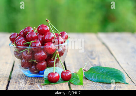 Rote reife Kirsche Früchte mit dem Stiel in Glasschale auf alten Brettern Stockfoto