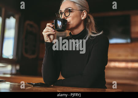 Eine nachdenkliche Seniorin sitzt im Café und trinkt Kaffee. Geschäftsfrau in Casuals trinkt eine Tasse Kaffee. Stockfoto