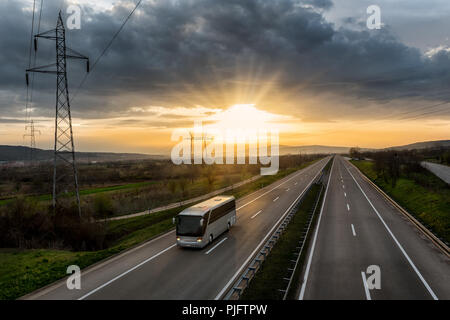 Bus Reisen auf eine einsame Landschaft Autobahn mit dem Sonnenuntergang hinter Stockfoto