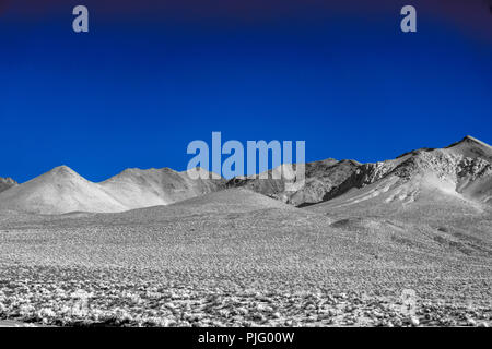 Unfruchtbare wüste Tal mit Bergen im Hintergrund unter einem klaren blauen Himmel. Stockfoto