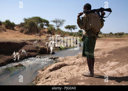 Eine bewaffnete Turkana junge Mann wacht über die Herde von Ziegen ist das Trinken von einem Fluss in der Nähe von Isiolo im Norden Kenias, 28. März 2012. Stockfoto