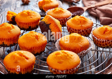 Frisch gebackene leckere Süße Kürbis Muffins auf einem runden Edelstahl Kuchen Kühlung Rack auf einem rustikalen Holztisch, leckere Herbst Dessert für Hal Stockfoto