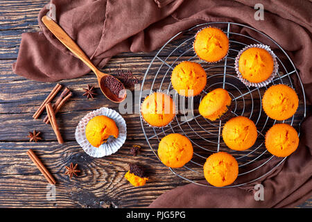 Frisch gebackene hausgemachten süßen Kürbis Muffins auf einem runden Edelstahl Kuchen Kühlung Rack auf einem rustikalen Holztisch, leckere Herbst Dessert für Halle Stockfoto