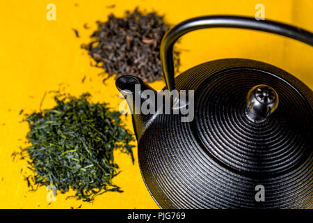 Gusseisen Teekanne (tetsubin) mit losen Blatt schwarzer und grüner Tee Stapel vor gelbem Hintergrund Stockfoto
