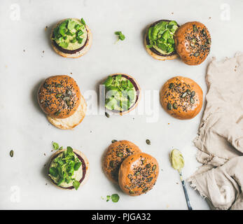 Flachbild-lay der gesunden veganen Burger mit Quinoa Rote-bete-Bratlinge, Avocado Creme und Grün sprießt auf hellen Hintergrund, Ansicht von oben. Vegetarisch, sauber ea Stockfoto