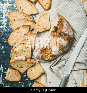 Flachbild-lay mit frisch-gebackenem Sauerteig Brot aus Weizen Brot halbieren und in Scheiben über Bettwäsche Serviette und rustikalen Tisch Hintergrund ausschneiden, Ansicht von oben, Quadrat Erntegut Stockfoto