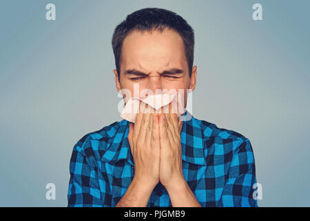 Kranken Mann isoliert hat Schnupfen. Ein junger Kerl niest in einem rosa Schal auf blauem Hintergrund. Erkältungen im Herbst. Stockfoto