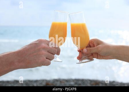 Hände, die Gläser mit Cocktail gegen ein Meer Stockfoto