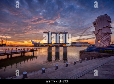 Skyline von Singapur bei Sonnenaufgang, mit der Merlion, das Marina Bay Sands, der Kunst und Wissenschaft Museum und der Singapore Flyer, alle unter einem dramatischen Himmel. Stockfoto