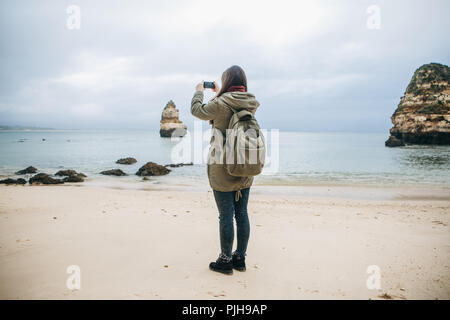 Mädchen mit einem Rucksack Touristen fotografieren eine schöne Landschaft an der Atlantikküste. Stockfoto