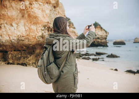 Mädchen mit einem Rucksack Touristen fotografieren eine schöne Landschaft an der Atlantikküste. Stockfoto