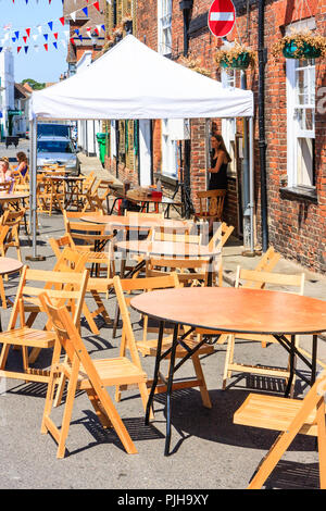 Leere Tische und Stühle draußen auf der Straße vor dem Café, Pub, im hellen Sonnenschein, für Ereignis später am Tag. Folk und Ale-Festival, Sandwich Stadt. Stockfoto
