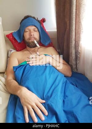Ein Mann mittleren Alters mit einem Bart ist krank mit einem Thermometer. Stockfoto